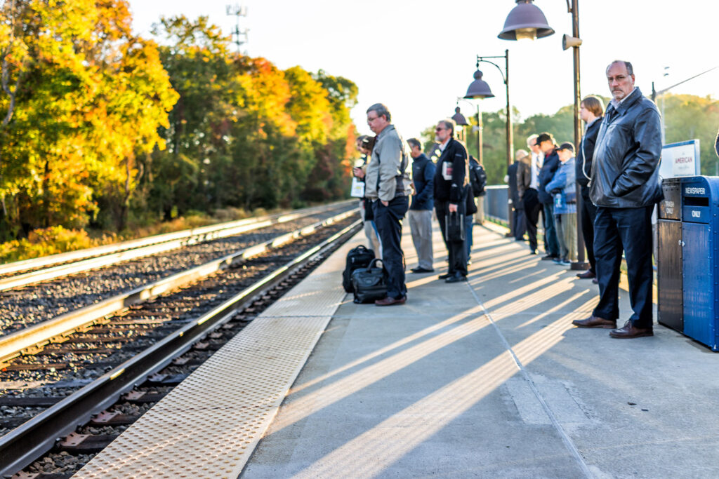 Group of people standing on an outdoor platform waiting for a train to arrive.